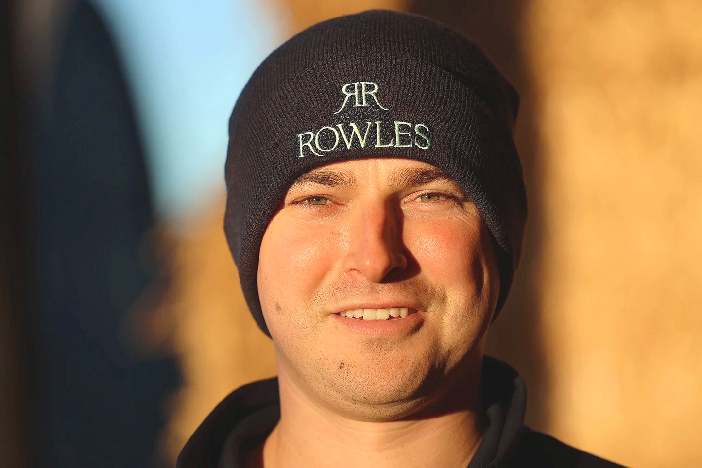 Person wearing a black beanie with 'RR Rowles' logo against a blurred background