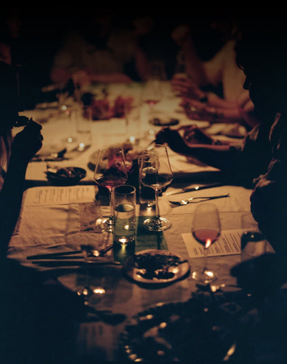 Dinner table set with wine glasses, cutlery, and plates in a dimly lit setting.