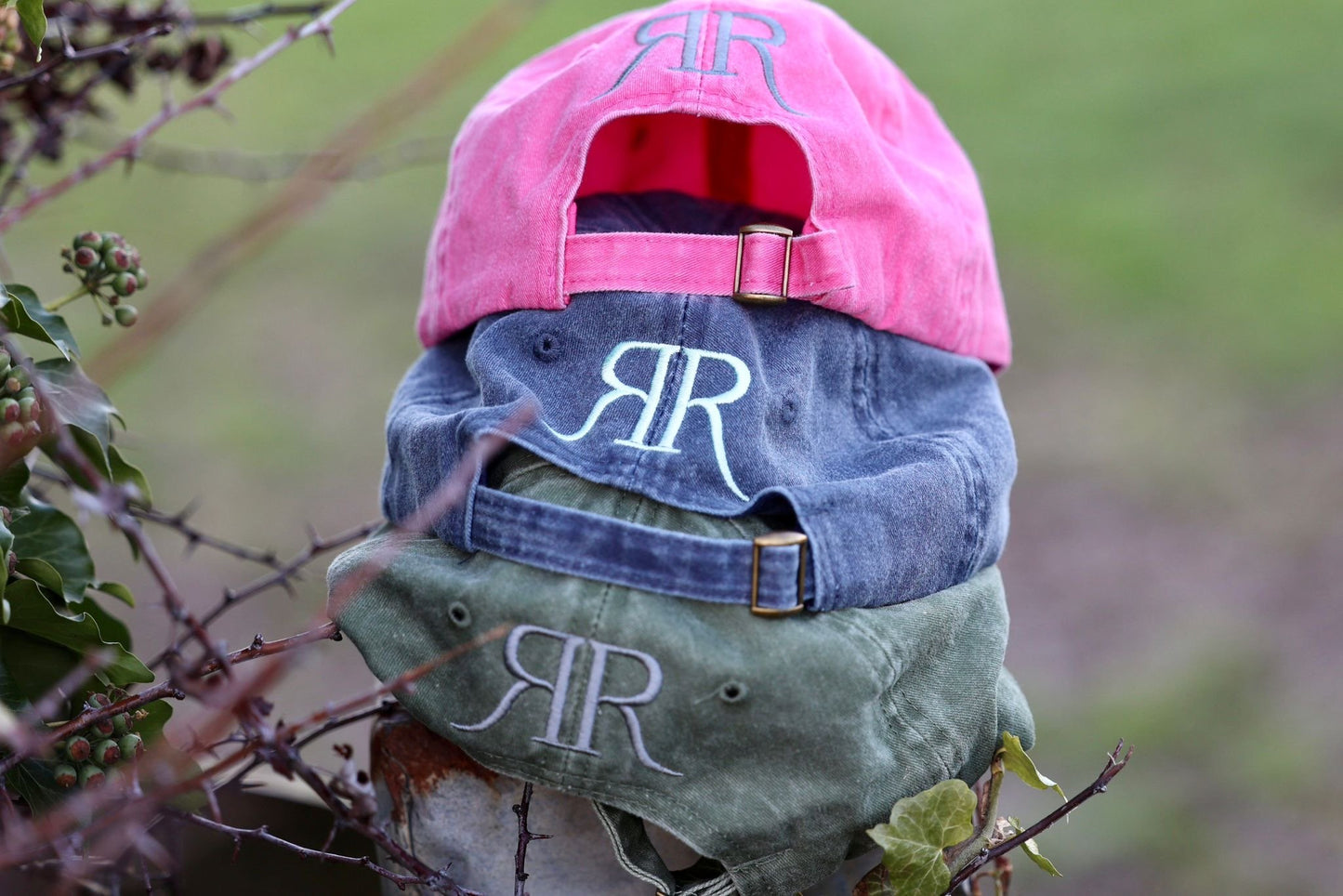 Three baseball caps with 'RR' monogram on a natural background