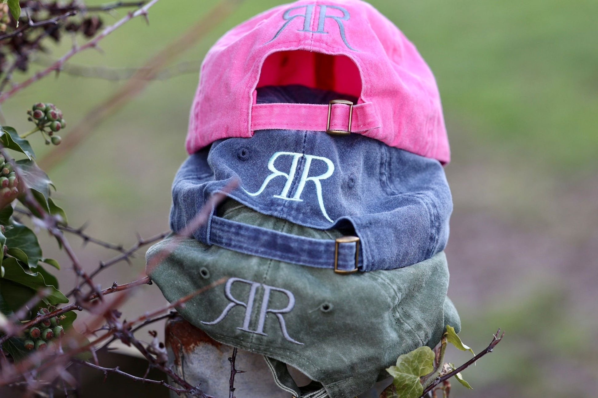 Three baseball caps with 'RR' monogram on a natural background