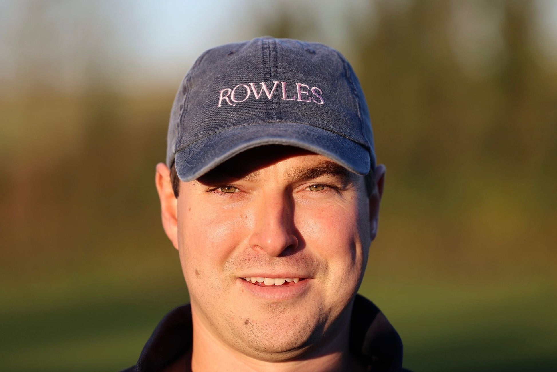 Man wearing a blue cap with 'ROWLES' branding outdoors