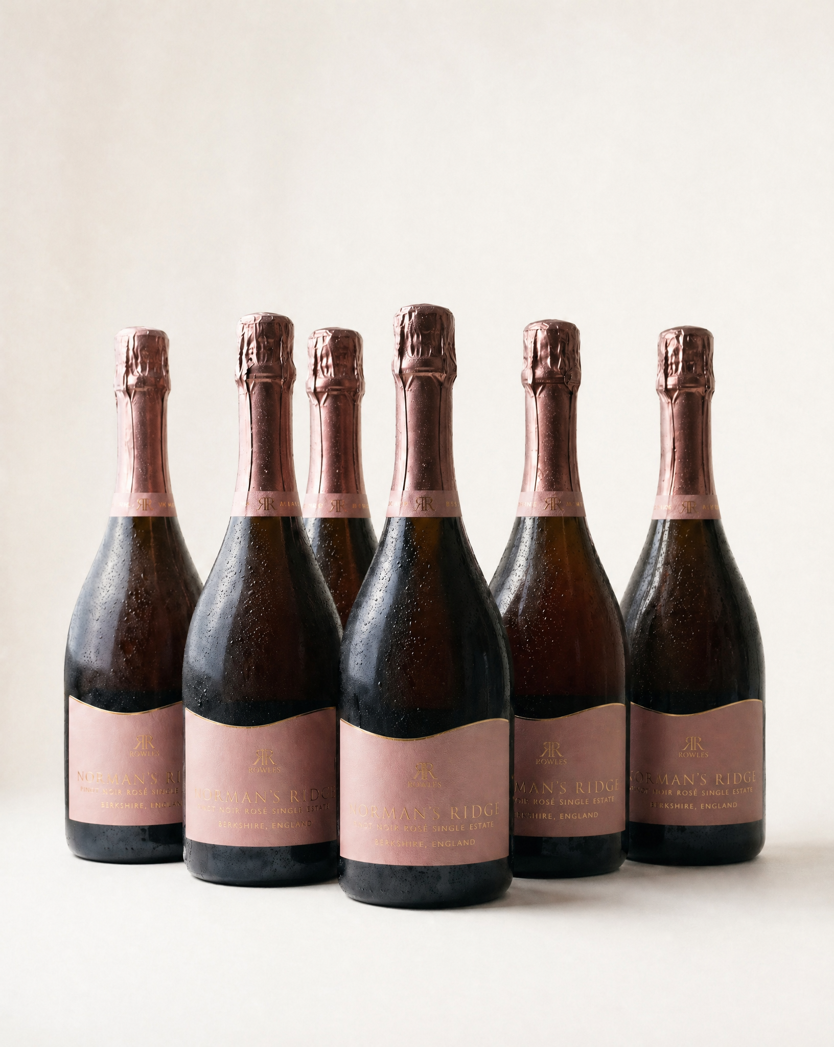 Six bottles of english sparkling rose with pink labels on a white background