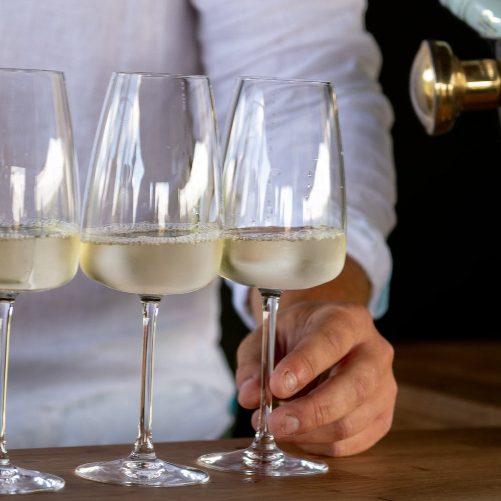 Person pouring white wine into three glasses on a wooden surface.