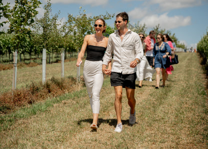 Two people walking hand in hand through a vineyard with other visitors in the background.