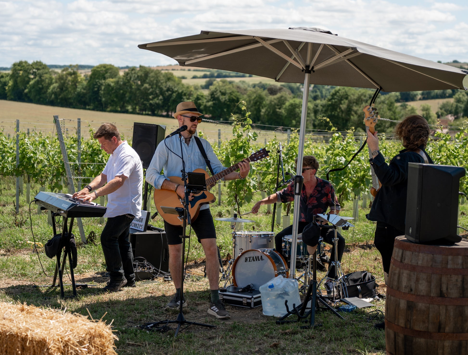 Band performing outdoors under a large umbrella with a scenic background