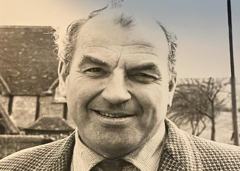 Black and white photo of a man wearing a patterned jacket and tie outdoors.