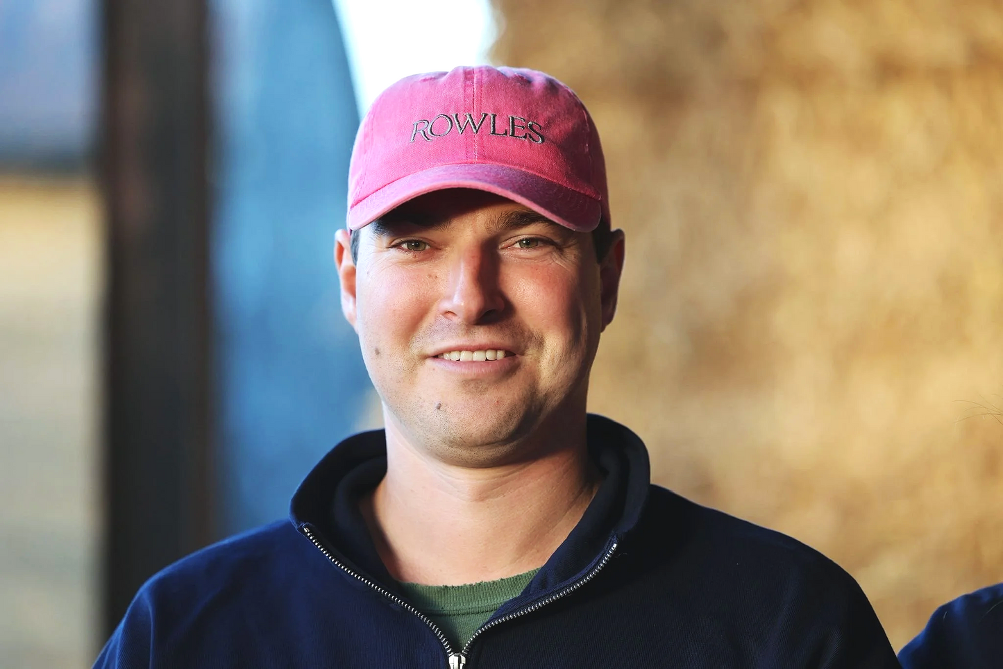 Man wearing a pink cap with 'Rowles' branding, standing against a blurred background.