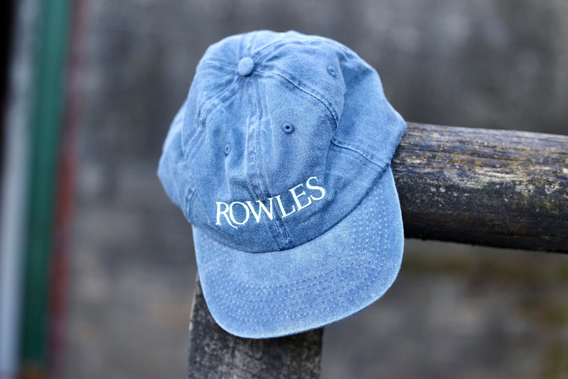 Blue cap with 'ROWLES' logo on a wooden post against a blurred background