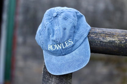 Blue cap with 'ROWLES' logo on a wooden post against a blurred background